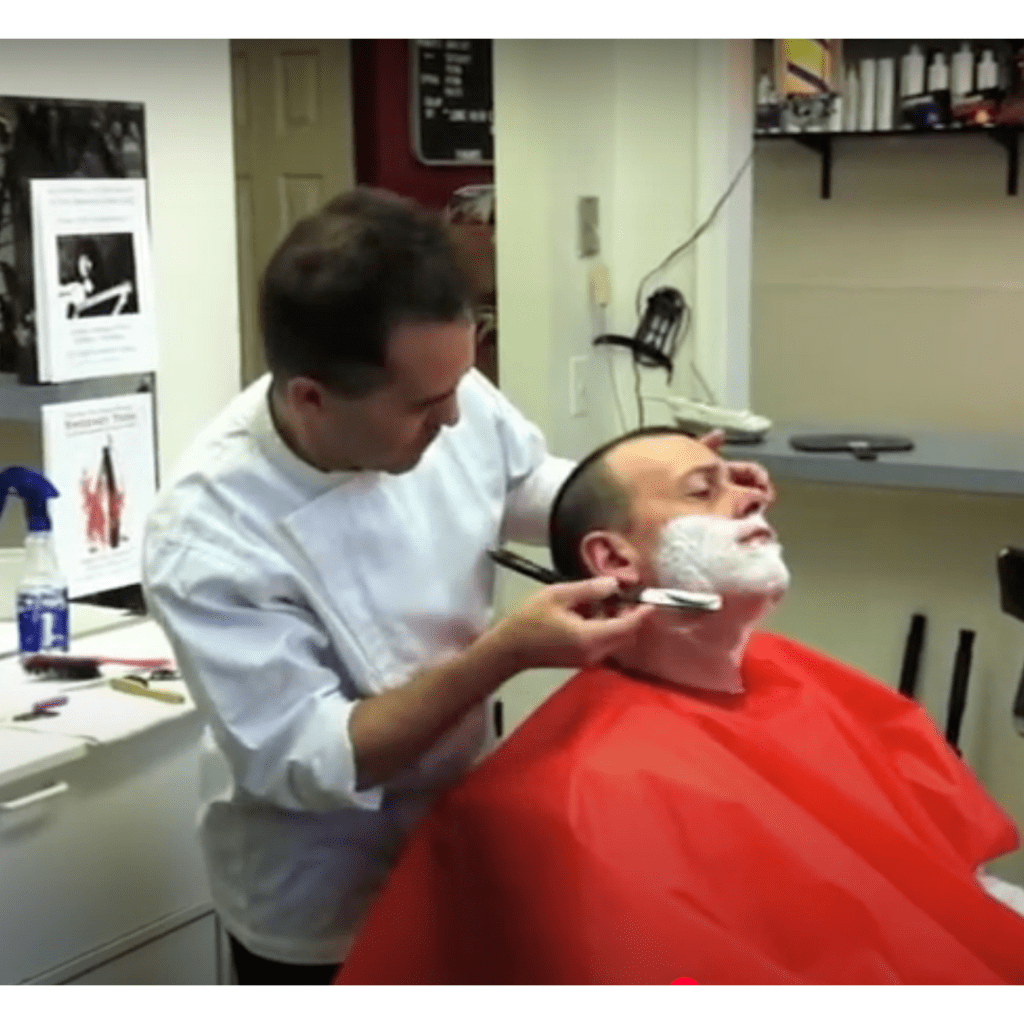 barber shaving a man who is wearing a red protection poncho