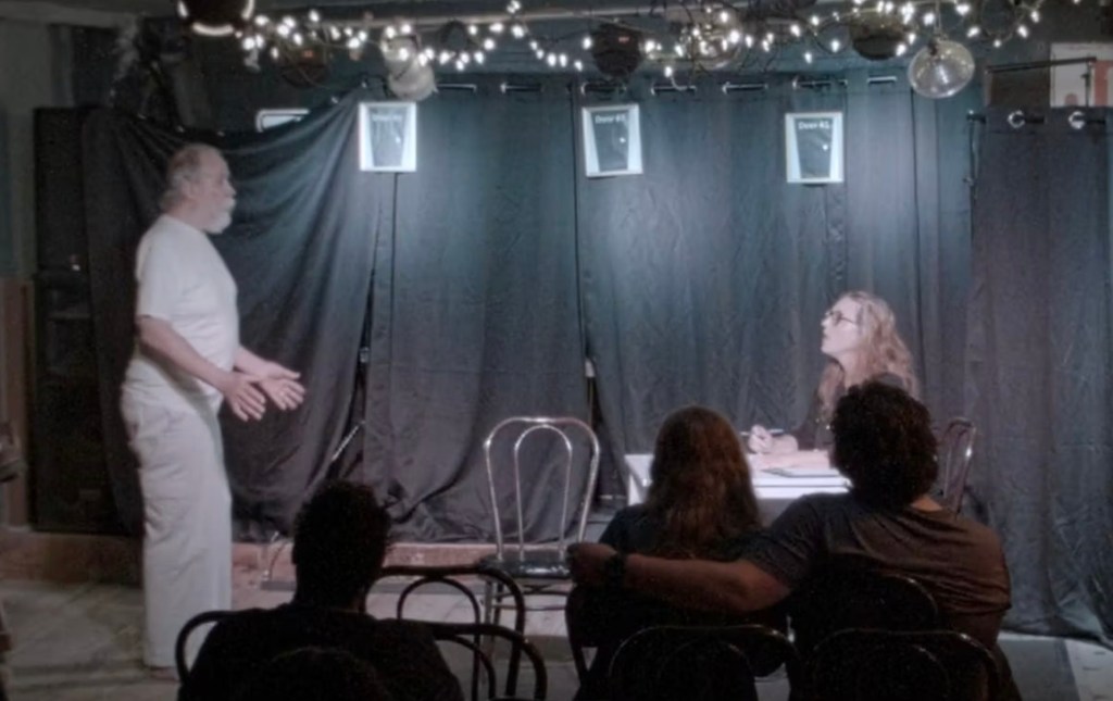 expiration date play woman sitting and man standing with lights and a black curtain as backdrop